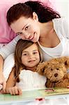 Portrait of mother and daughter reading a book together in bed