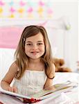 Little girl reading a book sitting in bed