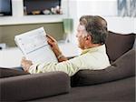 senior man sitting on sofa and reading newspaper