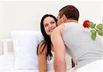 Man holding a rose giving a kiss to his beautiful wife in bed