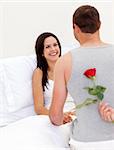 Husband surprising his beautiful wife with a rose in bed