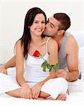 Man kissing a woman and holding a rose in bed