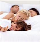 Little boy smiling on bed wile his parents and sister sleep