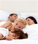 Little girl smiling on bed wile her parents and brother sleep