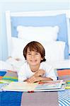 Smiling little boy reading a book in bed