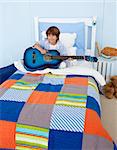 Happy little boy playing guitar in bedroom
