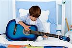 Happy little boy playing guitar in bed