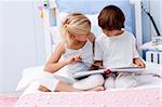 Little brother and sister reading a book in bed