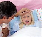 Father checking his daughter's temperature in bed