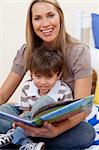 Smiling motherr reading a book with her son in bedroom