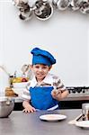 Little boy with blue hat and apron baking in the kitchen