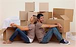 Happy couple sitting on floor unpacking boxes after moving house