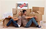 Happy couple sitting on floor after moving house with boxes around