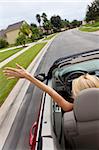 A beautiful young blond woman driving her convertible car with her hand in the air feeling the wind blowing