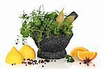 Fresh and dried mixed herb leaf selection in a granite mortar with pestle with lemons oranges, star anise and peppercorns, over white background with reflection.