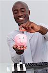 Afro-American businessman saving money in a piggybank in the office