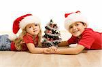 Kids with small decorated tree and christmas hats laying on the floor - isolated