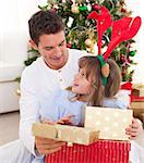 Portrait of a smiling father and his daughter opening Christmas presents in the living-room
