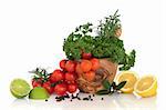 Herb leaves of parsley and rosemary with cherry tomatoes in an olive wood mortar with pestle with lemon and lime fruit halves, bay leaves and peppercorns, over white background.