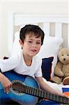 Portrait of a little boy playing guitar on bed