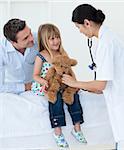 A doctor examining smiling child and playing with a teddy bear in the hospital