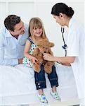 Female doctor and happy little girl examing a teddy bear in the hospital