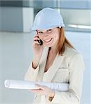 Smiling female architect with hardhat on phone in a building site