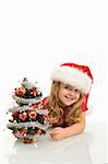 Smiling little girl peeking out a small christmas tree wearing a santa hat - isolated