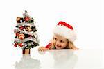 Happy kid with santa hat lurking around a small christmas tree - isolated