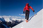 A male climber , dressed in red, climbs down a snowy slope. Winter clear sky day. In background the Monte Rosa massif, Italy, Europe.