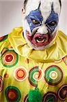 A nasty evil clown, angry and looking mean. Harsh lighting, focus on the teeth.