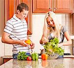 Young couple in the kitchen enjoy preparing salad with fresh vegetables. Square shot.