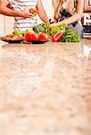 Young couple picks through fresh vegetables at the far end of a kitchen counter. Vertical shot.