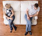 Man and a woman sit distantly on the ends of a cream colored love seat. Horizontal shot.