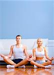 Young couple in sportswear sit on the floor meditating with closed eyes. Vertical shot.