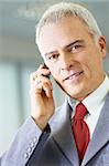 portrait of mature business man talking on the phone, looking at camera and smiling.