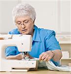 Older woman working on sewing machine. Square framed shot.
