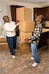Smiling senior african american man balancing moving boxes while his wife helps. Vertical shot.