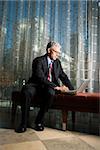 Businessman in suit sitting on a bench working on a laptop. Vertical shot.