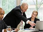 Businessman at meeting pointing to laptop.  Horizontally framed shot.