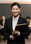 Businesswoman standing and smiling holding folder.  Vertically framed shot.