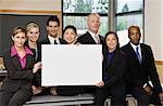 Business people in conference room smiling holding placard.  Horizontally framed shot.