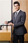 Businessman smiling standing next to reception desk.  Vertically framed shot.