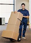 Young man using hand truck to move boxes.  Vertically framed shot.