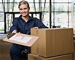 Young woman using hand truck to move boxes with delivery forms.  Horizontally framed shot.