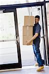 Young man delivering boxes through open door.  Vertically framed shot.