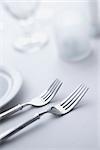 Two forks sitting side-by-side on a dining table with white tablecloth. Vertical shot.