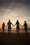 Silhouette of family holding hands on beach watching the sunset. Vertically framed shot.