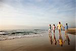 Family of four holding hands and walking on beach in North Carolina.