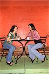 Two young adult women sitting in a cafe, having coffee and talking. Vertical shot.